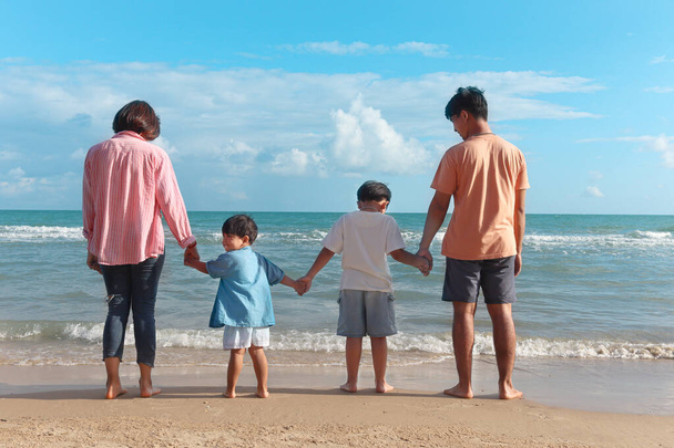 Famille heureuse quatre passer du temps et s'amuser ensemble pendant les vacances d'été, parents joyeux enfants se tiennent la main par derrière sur la plage de la mer tropicale, week-end de repos et de détente sur la plage.    - Photo, image