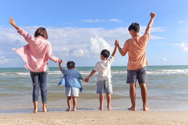 Happy family four spend time and have fun together on summer holiday vacation, cheerful parents children hold and raise hands up from behind on tropical sea sand beach, resting and relaxing weekend. - Photo, Image