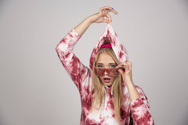 Młoda kobieta w różowych okularach ciągnąca sweter. Wysokiej jakości zdjęcie - Zdjęcie, obraz