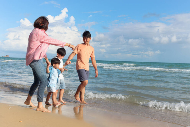 Szczęśliwa czteroosobowa rodzina spędza razem czas na wakacjach letnich, rodzice i dzieci trzymając się za ręce i spacerując tropikalną plażą morską, matka ojciec i dzieci odpoczywają i relaksują się w weekend.  - Zdjęcie, obraz