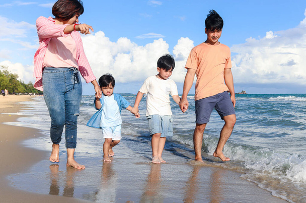 Une famille heureuse de quatre personnes passe du temps ensemble en vacances d'été, parents et enfants se tenant la main et marchant le long de la plage de la mer tropicale, mère, père et enfants se reposant et se relaxant le week-end.  - Photo, image
