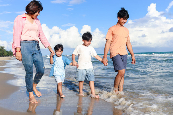 Happy family of four spend time together on summer holiday vacation, parents and children holding hand and walking along tropical sea beach, mother father and kids resting and relaxing on weekend.  - Photo, Image