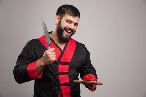 Positive man holding wooden board with red pepper and knife. High quality photo - Photo, Image