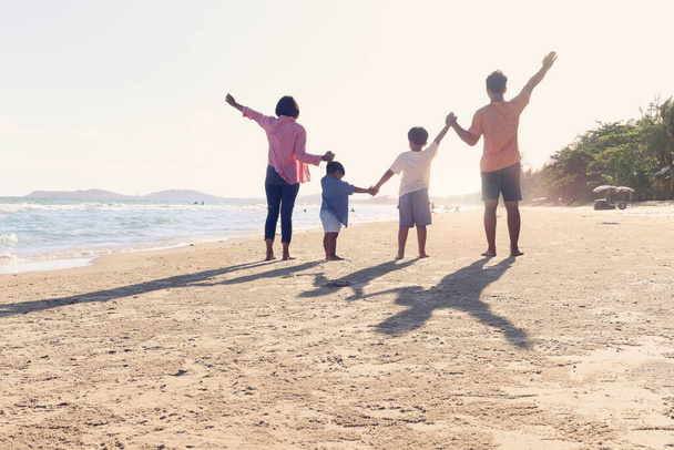 Happy family of four spend time and have fun together on summer holiday vacation, cheerful parents children hold and raise hand up from behind on tropical sea sand beach, resting and relaxing weekend. - Photo, Image
