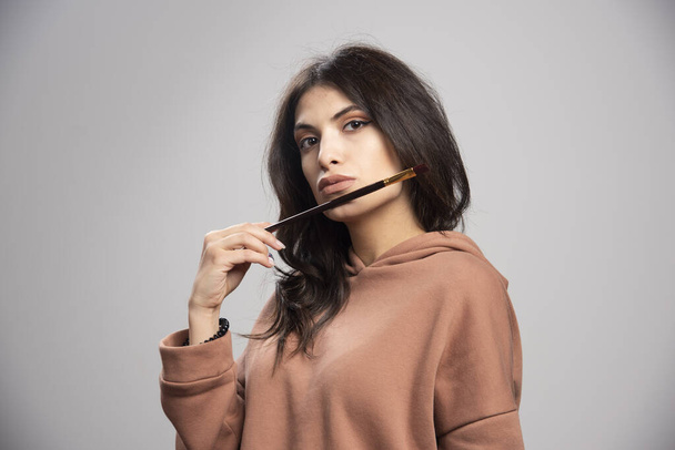 Young woman holding paint brush on gray background. High quality photo - Foto, Imagen