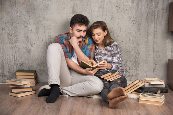Zdjęcie młodej pary siedzącej na podłodze i czytającej książkę. Wysokiej jakości zdjęcie - Zdjęcie, obraz