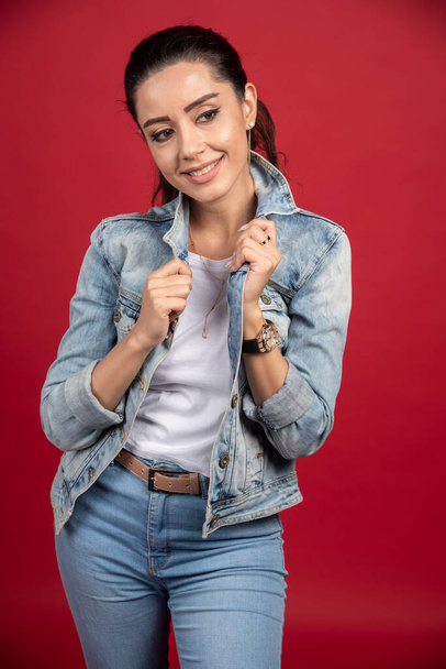 Positive woman in denim jacket standing on red background. High quality photo - Foto, Imagem
