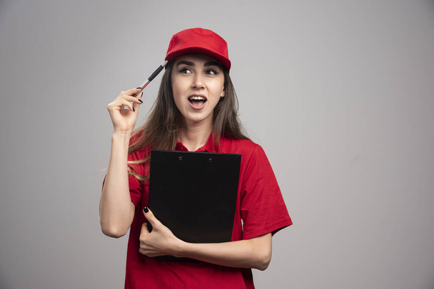 Dostawczyni w czerwonym mundurze trzymająca notatnik. Wysokiej jakości zdjęcie - Zdjęcie, obraz