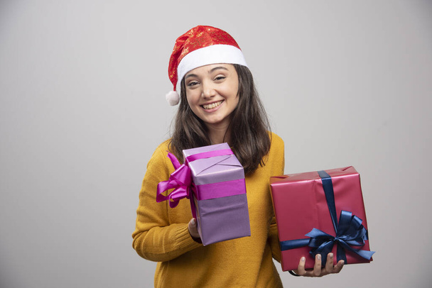 Νεαρή γυναίκα με καπέλο Αϊ Βασίλη που κρατάει κουτιά δώρων. Υψηλής ποιότητας φωτογραφία - Φωτογραφία, εικόνα