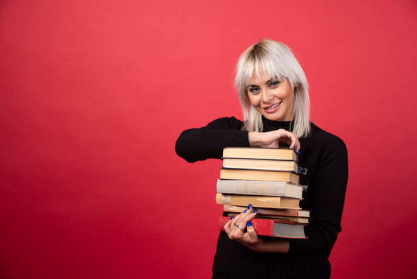 Young woman model carrying a lot of books on a red background. High quality photo - Foto, immagini