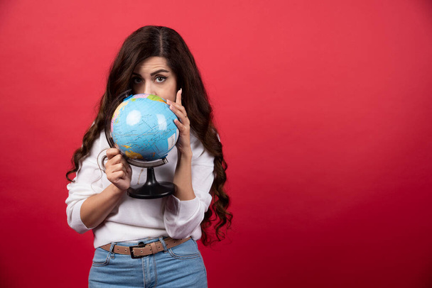 Brunette woman holding globe on red background. High quality photo - Foto, Imagen