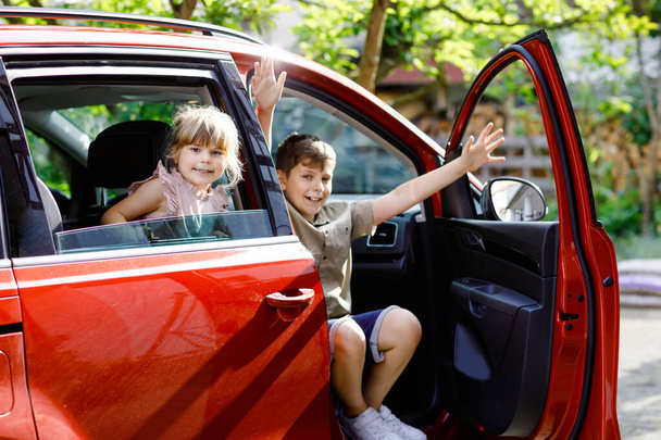 Two children, school boys sitting in car before leaving for summer vacation with parents. Happy kids, siblings, brothers and friends by windows of car going on journey, family road trip - Foto, Imagen