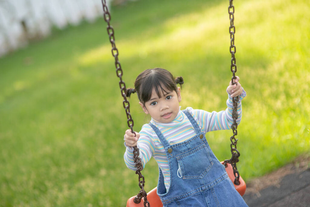 Ευτυχισμένο μικρό ασιατικό κορίτσι παίζει swing εξωτερική στο πάρκο - Φωτογραφία, εικόνα