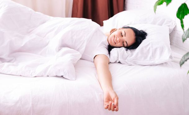 L'image d'une jeune fille souriante couchée dans un lit blanc comme neige dans la chambre. Mes yeux sont fermés.. - Photo, image