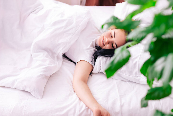 A imagem de uma jovem menina bonita sorridente deitada em uma cama branca de neve no quarto. Os meus olhos estão fechados. - Foto, Imagem