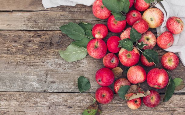 As maçãs vermelhas espalham-se em um tecido leve em uma mesa de madeira. Humor de outono, vibrações e cores de outono, moda e estilo de outono - Foto, Imagem