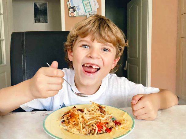 Маленький щасливий школяр, який їсть макаронну локшину та спагеті. Симпатична дитина з зубною щілиною на домашній домашній кухні, обідаючи після школи
. - Фото, зображення