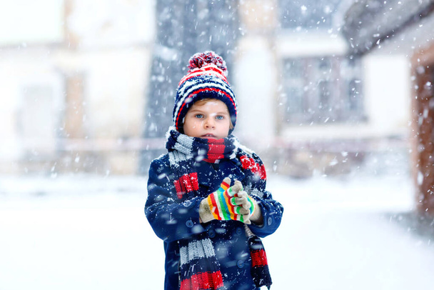 Χαριτωμένο μικρό αστείο παιδί σε πολύχρωμα ρούχα χειμερινής μόδας διασκεδάζοντας και παίζοντας με το χιόνι, σε εξωτερικούς χώρους κατά τη διάρκεια της χιονιού. Ενεργός ελεύθερος χρόνος σε εξωτερικούς χώρους με παιδιά. Παιδί αγόρι και μικρό παιδί πιάνει νιφάδες χιονιού. - Φωτογραφία, εικόνα