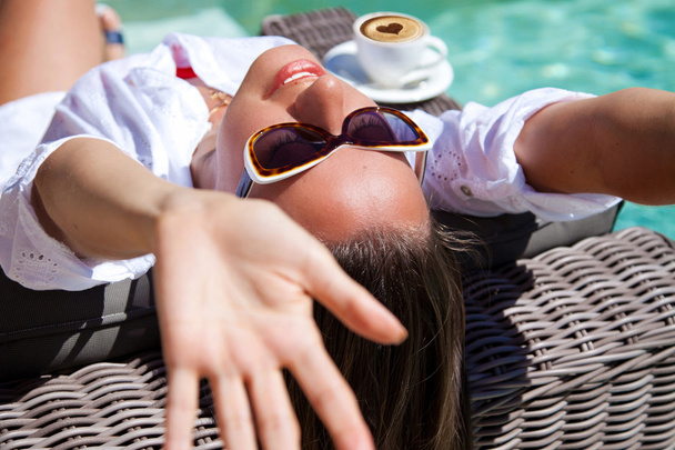 Happy young woman laying on chaise-longue poolside - Photo, Image