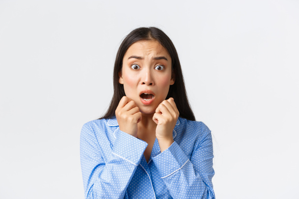 Close-up of scared asian woman in panic standing in pajama speechless, react to frightening and shocking scene, looking afraid, shivering from fear over white background - Photo, Image
