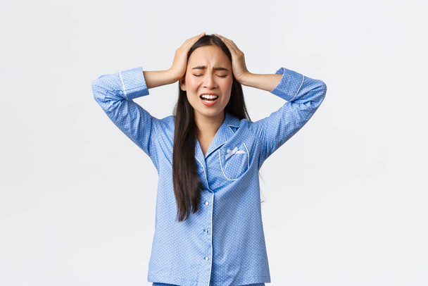 Harmillinen hälyttävä aasialainen tyttö sinisessä pyjamassa seisoo epätoivoinen ja ahdistunut, kädet pään päällä kieltäminen ja huutaminen, paniikki ja turhautuminen, jolla on suuri ongelma, valkoinen tausta - Valokuva, kuva