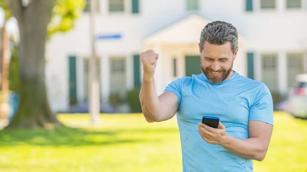 happy unshaven guy celebrating success reading good news on smartphone, copy space, happiness - Photo, Image