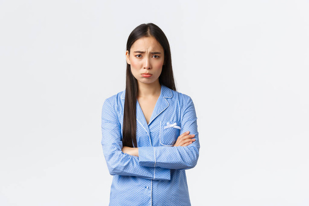 Uražená hloupá nejistá asijská dívka v modrém pyžamu, se zkříženýma rukama na prsou a vzlykající, trucující a mračící se z nespravedlivé situace, uražená a smutná, bojácná na bílém pozadí - Fotografie, Obrázek