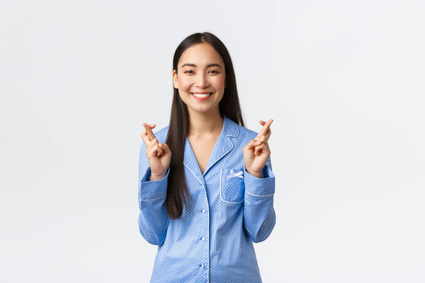 Šťastná usměvavá asijská dívka v modrém pyžamu s vírou ve sny se stane skutečností, kříž prsty hodně štěstí, dělat přání jako čeká na důležité výsledky, stojící bílé pozadí optimistické - Fotografie, Obrázek