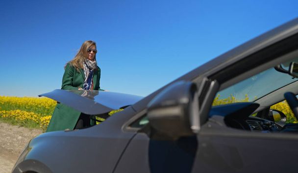 Женщина в пальто открывает капот автомобиля. - Фото, изображение