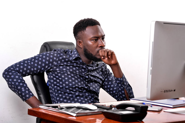 Portret młodego biznesmena siedzi w swoim biurze i pracuje z laptopem trzymając rękę nad ustami. - Zdjęcie, obraz