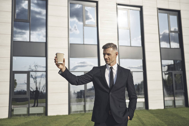 Confident mature businessman holding coffee cup while standing near office building - Fotoğraf, Görsel