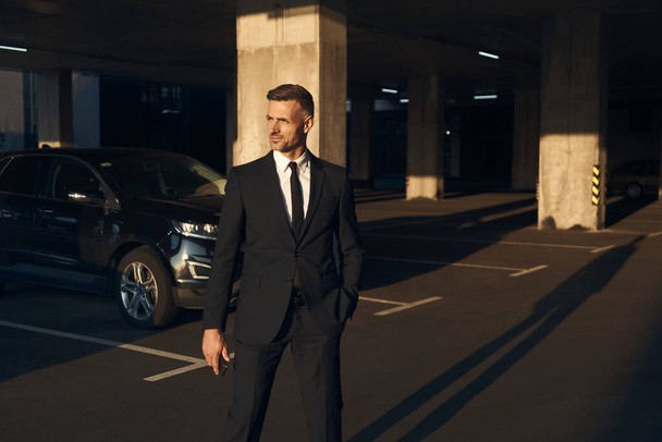 Confident mature man in full suit walking by parking lot - Fotó, kép