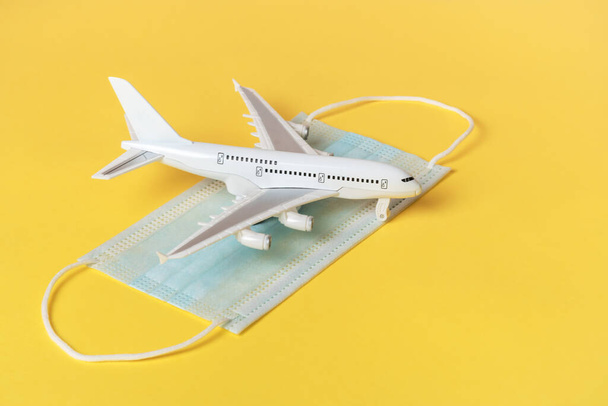 A toy white plane stands on a protective mask against illness. On a yellow background. Flight concept. - Foto, afbeelding