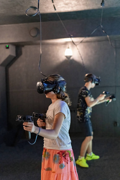 Una chica y un chico en cascos de realidad virtual con joysticks jugar juegos 3D de ordenador. - Foto, Imagen