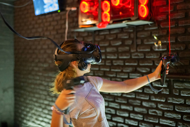Een meisje speelt in een virtual reality helm en houdt joysticks in haar handen tijdens het spelen van games in een computer club. Tiener esports-concept concurrentie. - Foto, afbeelding