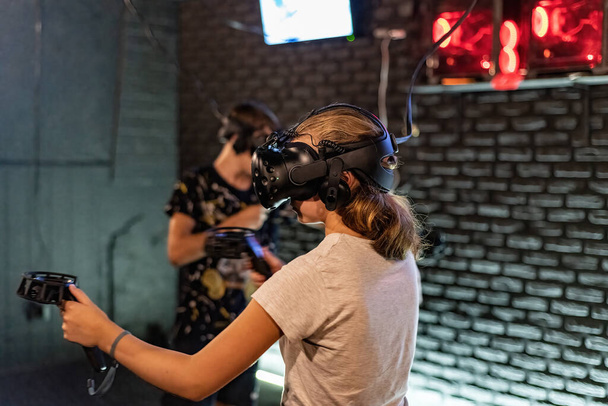 Ein Mädchen und ein Mann in Virtual-Reality-Helmen mit Joysticks spielen 3D-Computerspiele. - Foto, Bild