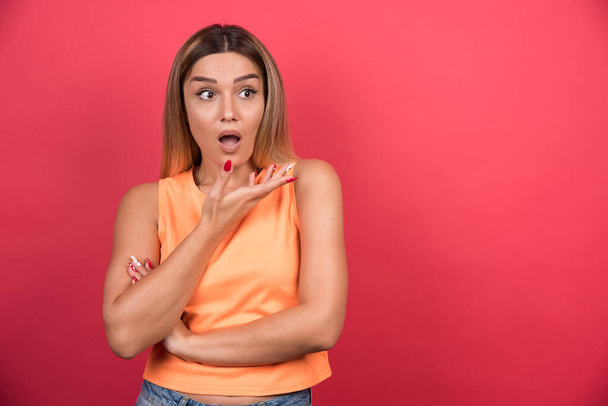 Confused young woman pointing her hand sideways on red background. High quality photo - Zdjęcie, obraz