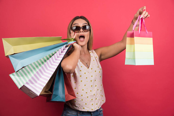 Glückliche Frau mit Brille, die ihre Einkaufstüten auf rotem Hintergrund hält. Hochwertiges Foto - Foto, Bild