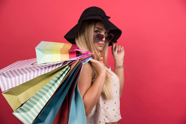 Woman in glasses and hat holding her shopping bags on red background . High quality photo - Photo, Image