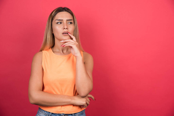 Displeased young woman keeping her hand on her chin on red background. High quality photo - Photo, Image