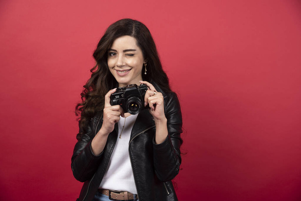 Beautiful woman photographer holding photo camera on a red background. High quality photo - Photo, Image