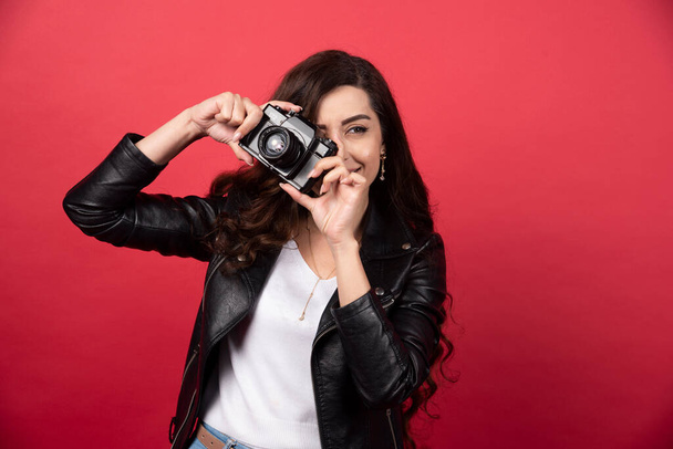 Γυναίκα φωτογράφος τραβά φωτογραφίες με μια φωτογραφική μηχανή σε κόκκινο φόντο. Υψηλής ποιότητας φωτογραφία - Φωτογραφία, εικόνα