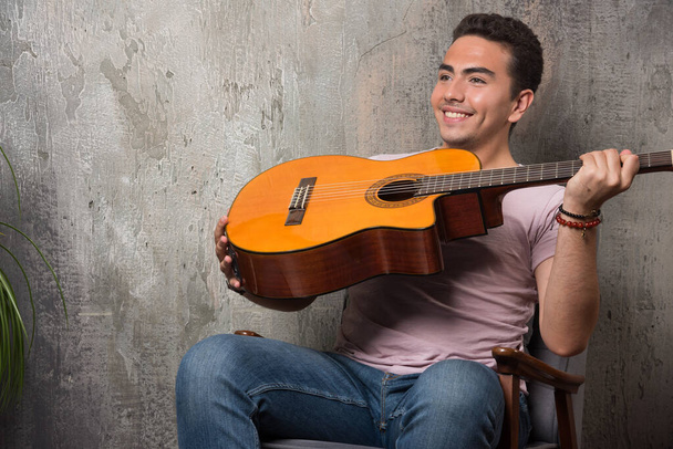 Musicista sorridente che tiene la chitarra su sfondo di marmo - Foto, immagini