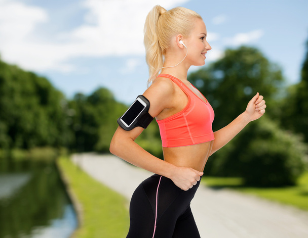 sporty woman running with smartphone and earphones - Фото, изображение