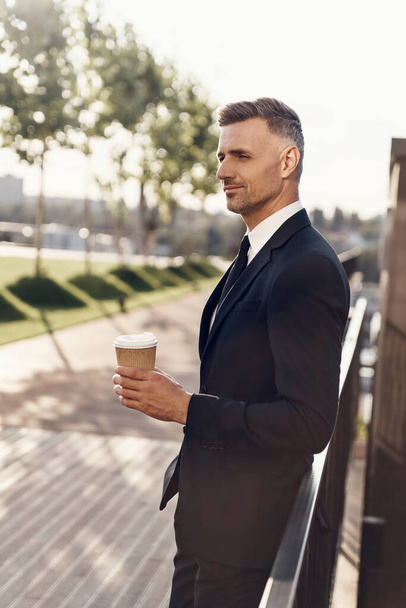 Confident mature businessman holding coffee cup while standing outdoors - Valokuva, kuva