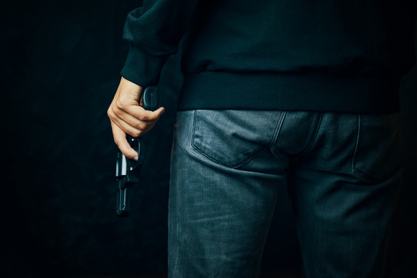 Muž v tmavém oblečení drží zbraň.. - Fotografie, Obrázek