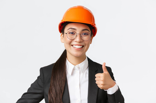 Detailní záběr profesionálního potěšené asijské ženské hlavní inženýrka, architektka v obleku a bezpečnostní přilba ukazující palec-up ve schválení, dát svolení, doporučit stavební společnost - Fotografie, Obrázek