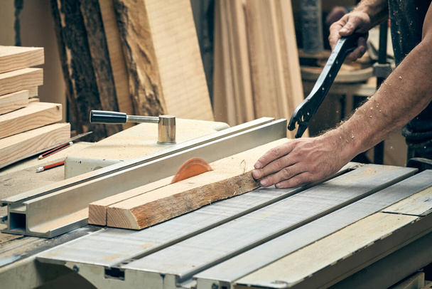 A closeup of a carpenter working on a circular saw. The process of cutting a wooden board. - Фото, зображення