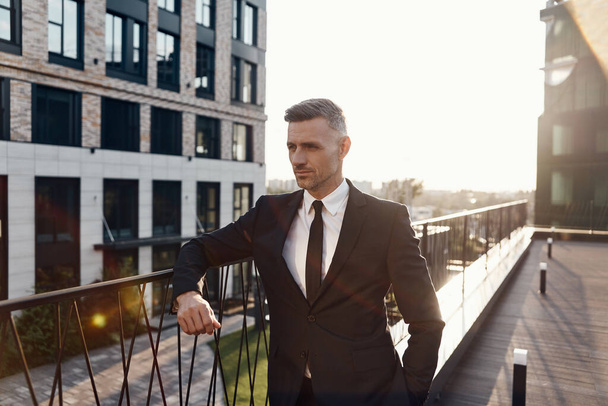 Confident mature man in full suit standing on business center terrace - Foto, Bild