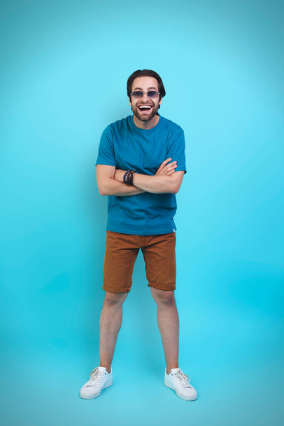 Excited young man in casual clothing gesturing and smiling while standing against yellow background - Фото, изображение